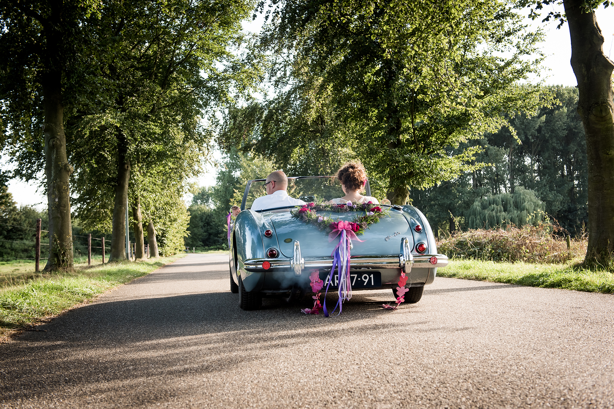Echte momenten trouwfotograaf: bruidspaar rijdt weg met trouwauto